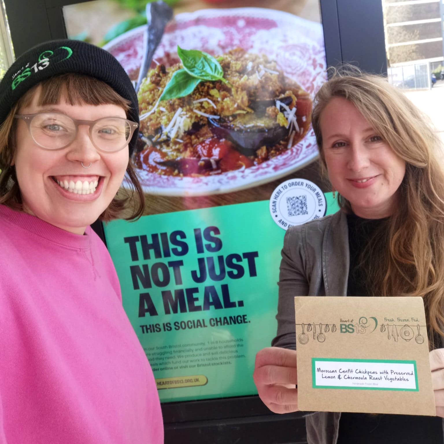 Heart of BS13 ready meal packaging being held by two smiling ladies at bus shelter advert behind.